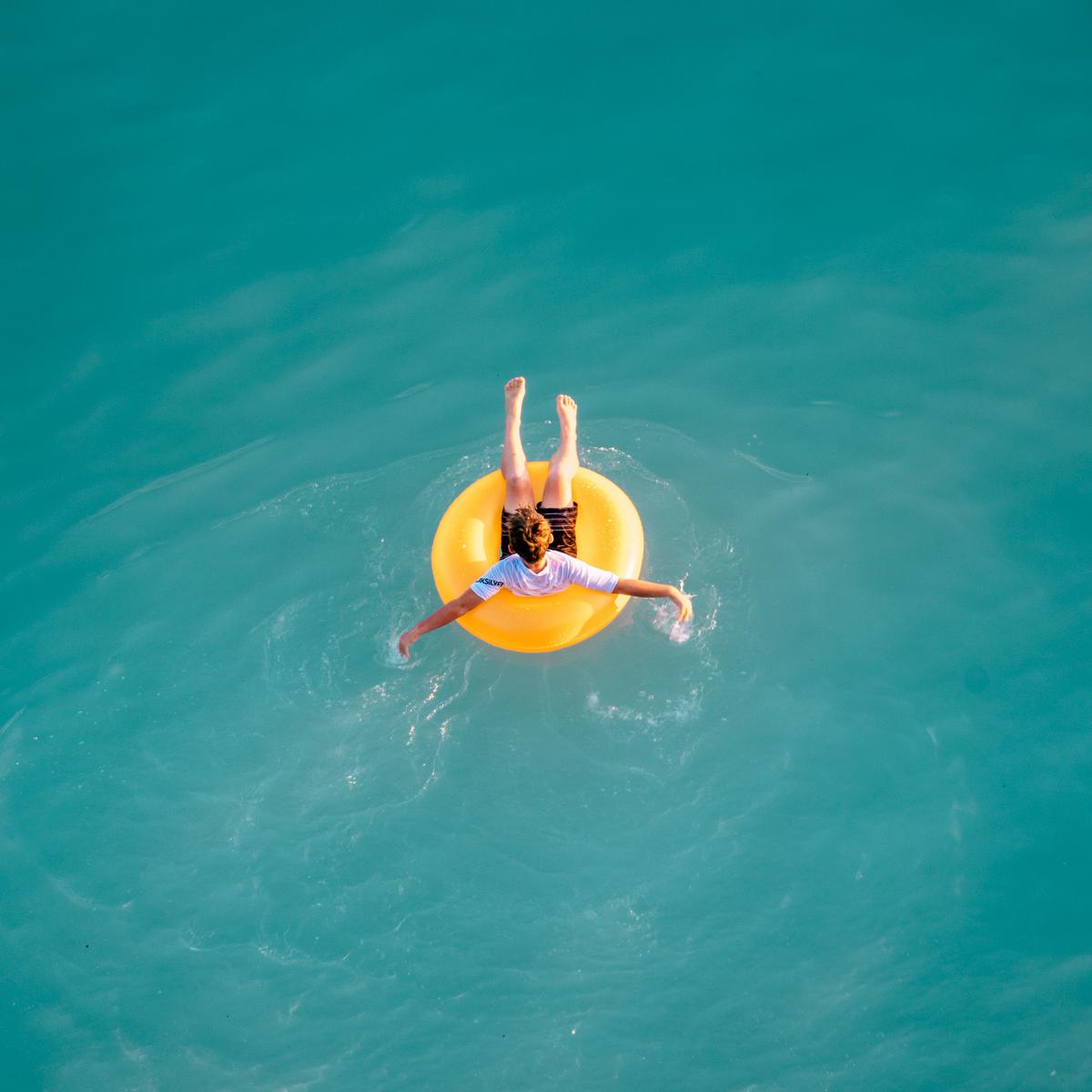穏やかな海の上で浮き輪で揺られる男の画像